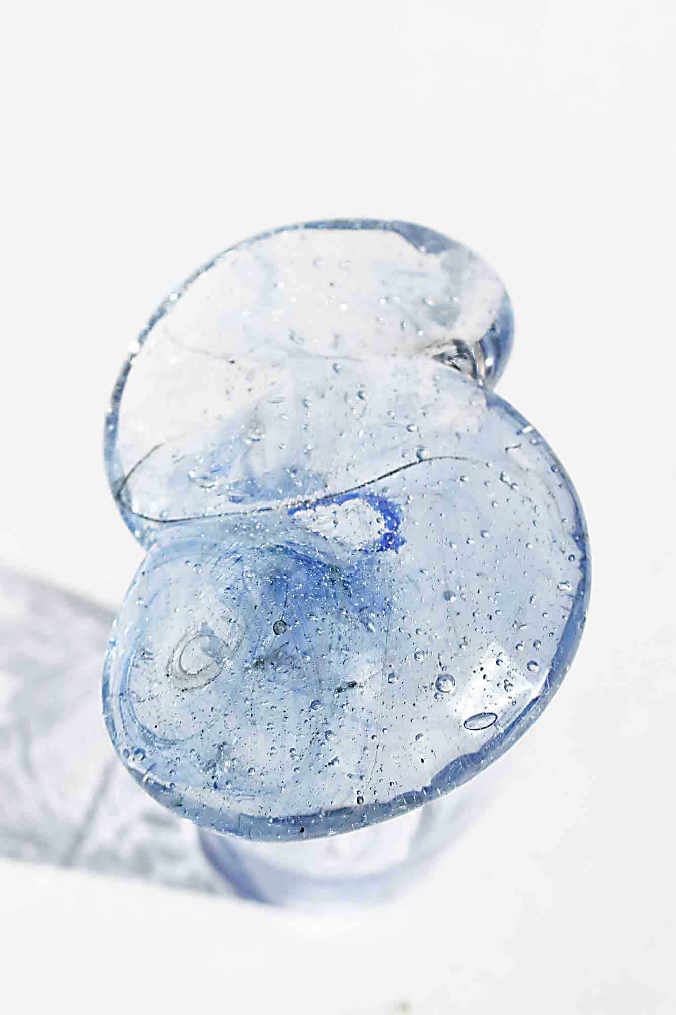 泡や青いすじ、小さな粒が混ざった淡い水色のアップサイクルグラス